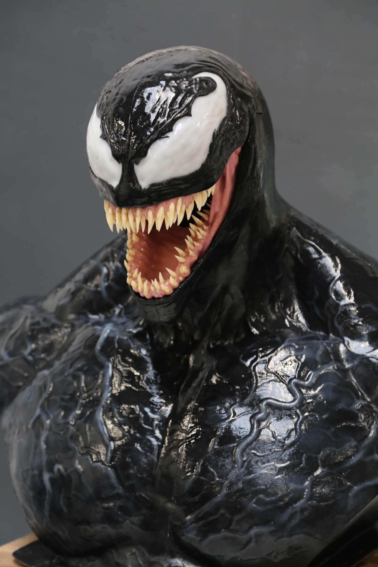 A detailed sculpture of Venom, a muscular black creature with sharp teeth, a wide open mouth, and large white eyes from Marvel comics, serves as an excellent VFX reference against a plain gray background.