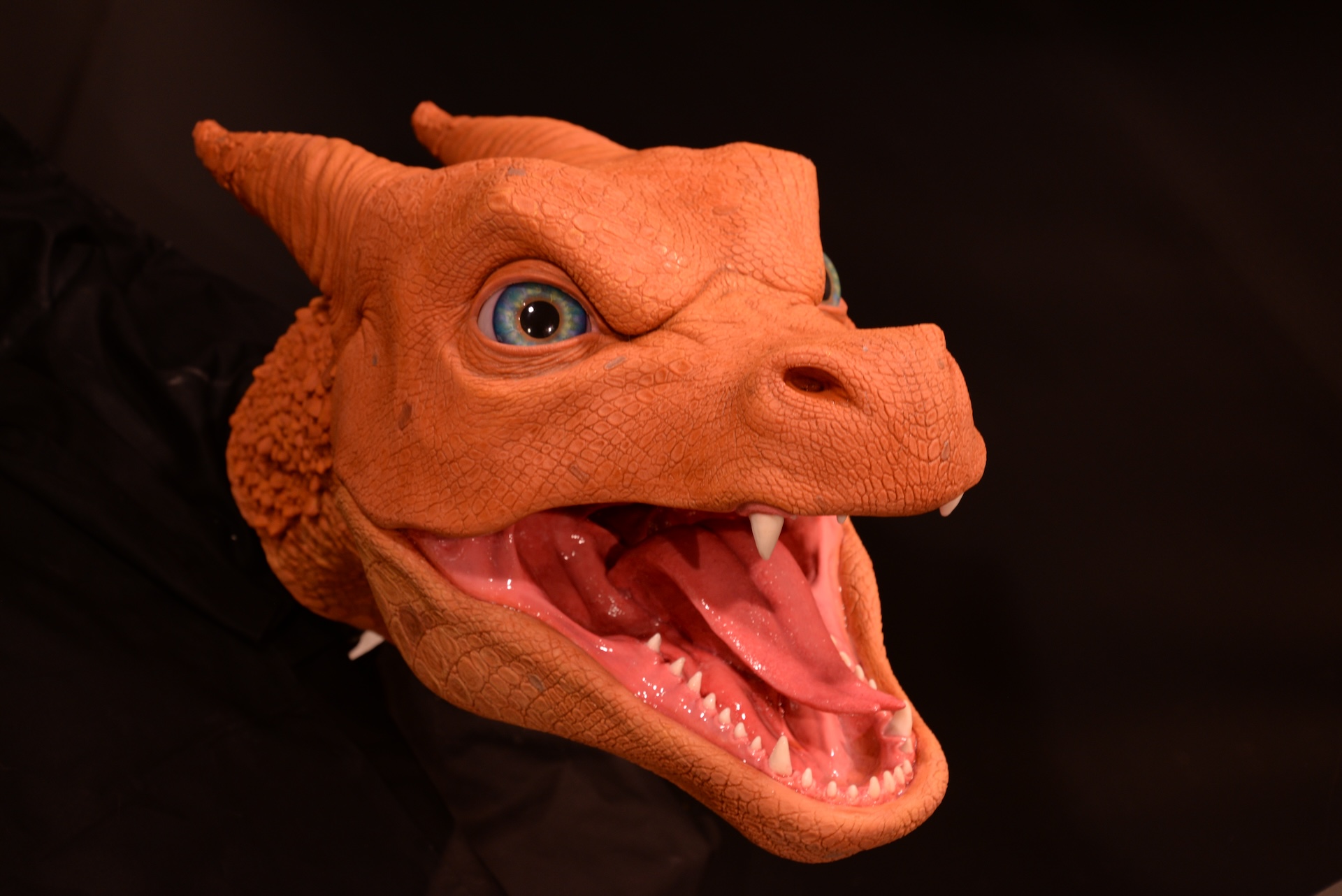 A realistic, orange dragon head model with blue eyes, open mouth, visible teeth, and sharp fangs against a dark background—ideal as a VFX reference.
