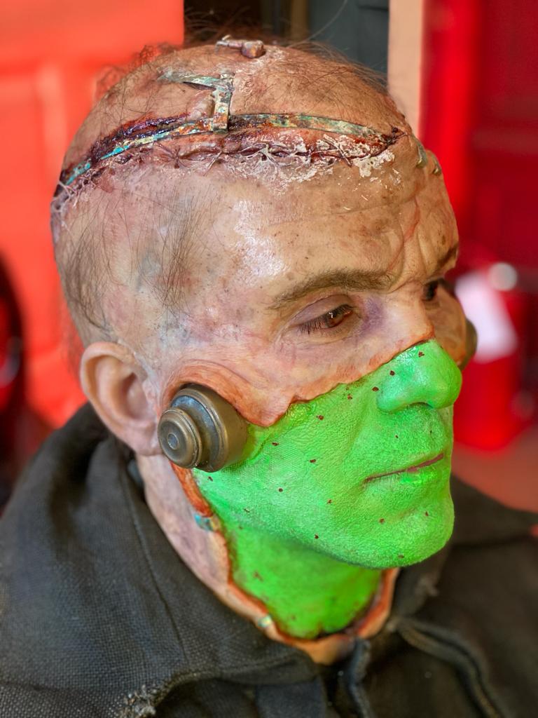 A person wearing realistic Frankenstein’s monster makeup, with a stitched scalp and metal bolts on the neck, serves as an excellent VFX reference for classic horror—featuring a bright green lower face.
