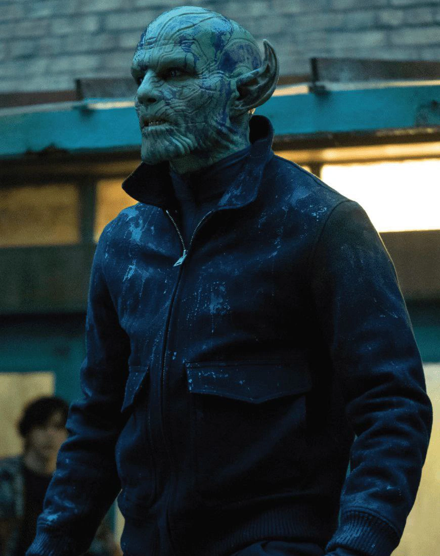 A humanoid alien with green, scaly skin, pointed ears, and blue markings wears a dark, paint-splattered jacket enhanced by KM Effects, standing outdoors in front of a building with a blurred person in the background.